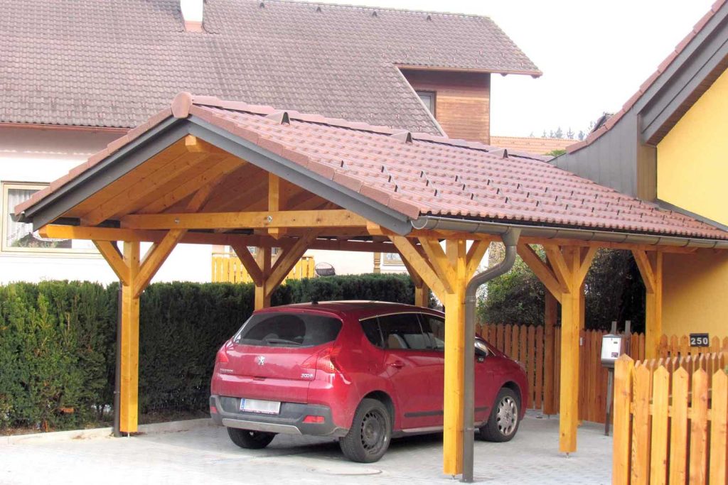 Carport aus Holz mit Satteldach und Ziegeldeckung, darunter ein rotes Auto