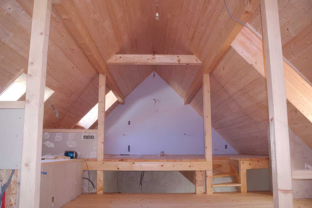 Dachraum im Rohbau mit sichtbaren Holzsparren, Holzverkleidung und Dachfenstern beim Dachausbau