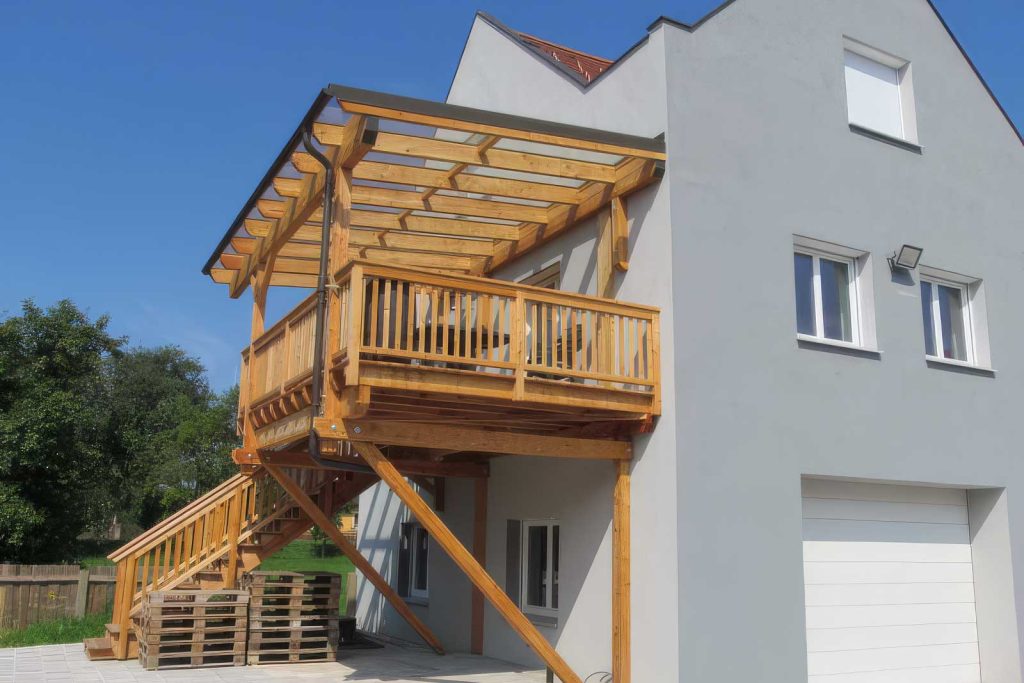 Terrassenüberdachung aus Holz über einem Balkon mit Holzgeländer und Außentreppe an einem Wohnhaus
