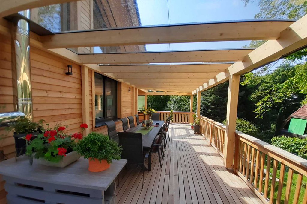 Große Holzterrasse mit Glasdach auf Holzkonstruktion, Holzgeländer, Esstisch und Blumen