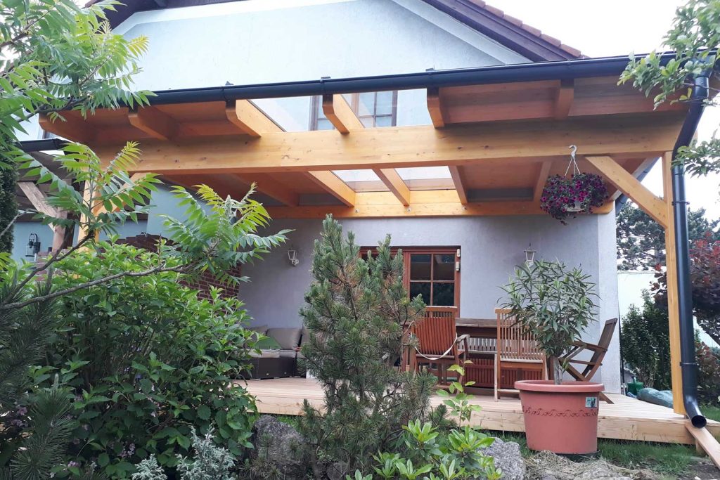Terrassenüberdachung aus Holz mit Glasdach an einem Wohnhaus, davor ein Garten